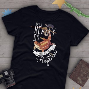 Könnte beinhalten: Schwarzes T-Shirt mit einer weißen Grafik eines Bartagamen, einer Schlange und einer Schildkröte. Der Text auf dem Shirt lautet "Ja, ich brauche wirklich all diese Reptilien."