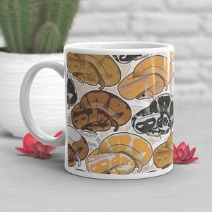 May include: White ceramic mug with a pattern of various colored snakes. The snakes are curled up in a variety of positions and are all different colors, including brown, tan, and black.