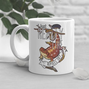 May include: White ceramic mug with a graphic of a bearded dragon, snake, and turtle. The text on the mug reads "Just Really Like Reptiles Ok?"
