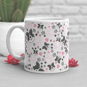 May include: White ceramic mug with a pattern of black and white border collie dog faces, pink paw prints, pink hearts, and gray stars.