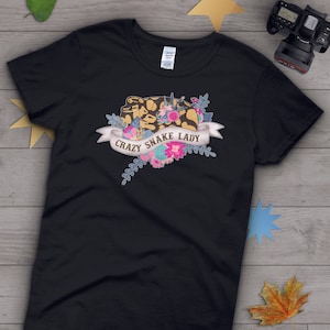 May include: Black t-shirt featuring a graphic of a snake with flowers and the text "Crazy Snake Lady".