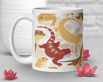Puede incluir: Taza de cerámica blanca con un patrón repetido de lagartos de dibujos animados en tonos marrón, beige y rojo. La taza tiene un asa curva y un acabado liso y brillante. El fondo es de color beige claro.
