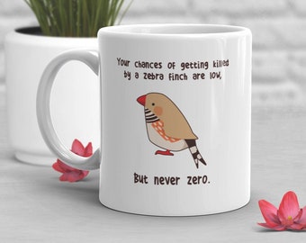 May include: White ceramic mug with a handle, featuring a cartoon zebra finch illustration. The text reads, "Your chances of getting killed by a zebra finch are low, but never zero."