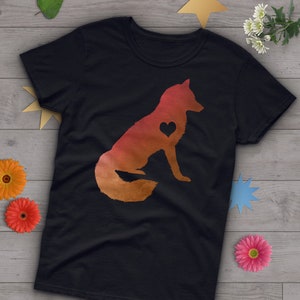 以下が含まれることがあります： 赤い、オレンジ、黄色のグラデーションで描かれたキツネのシルエットがプリントされた黒いTシャツ。キツネは尻尾を体の周りに巻き付けて座っており、胸にハートマークがあります。