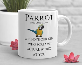 May include: White ceramic mug with a blue and yellow parrot illustration. The mug has the text "PARROT [PAR-UHT] NOUN A TIE-DYE CHICKEN WHO SCREAMS ACTUAL WORDS AT YOU."