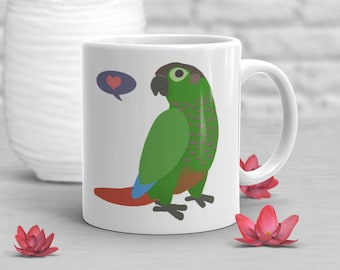 May include: White ceramic mug featuring a green and brown parrot illustration with a heart-shaped thought bubble. The parrot has a red tail and blue accents. The mug is on a gray surface with decorative flowers.