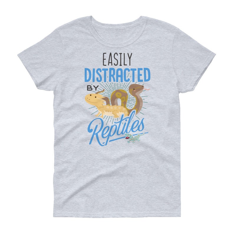 Może przedstawiać: Jasnoszary t-shirt z napisem "Easily Distracted By Reptiles" w kolorze niebieskim. Tekst jest otoczony wzorem promieni słonecznych. Są ilustracje węża i jaszczurki.