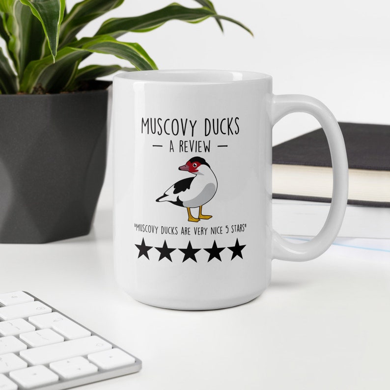 May include: White ceramic coffee mug with a black and white illustration of a Muscovy duck. The text "Muscovy Ducks - A Review -" is printed on the mug, along with the text "Muscovy Ducks are very nice 5 stars" and five black stars.