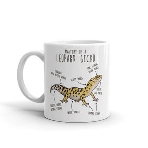 Puede incluir: Taza de cer&aacute;mica blanca con una ilustraci&oacute;n de dibujos animados de un gecko leopardo y un diagrama anat&oacute;mico humor&iacute;stico. El texto dice "Anatom&iacute;a de un gecko leopardo" e incluye etiquetas para las partes del cuerpo del gecko, como "Dispositivo de liberaci&oacute;n r&aacute;pida de emergencia", "Marcas de belleza", "Visiones de frijoles que miran el alma", "Portal de bichos sonrientes", "Almacenamiento de grasa majestuosa y regordeta", "Dep&oacute;sito de refrigerios" y "Troncos de zoom".