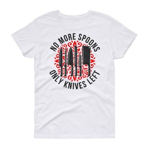 Puede incluir: Camiseta blanca con un dise&ntilde;o circular rojo que presenta un conjunto de cuchillos y el texto "No More Spoons Only Knives Left".