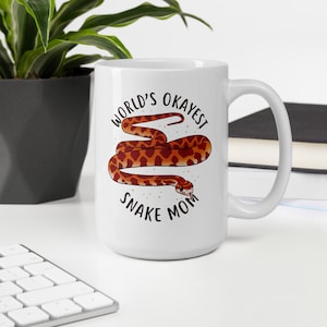 May include: White ceramic mug with a black and white graphic of a snake with the text "World's Okayest Snake Mom".