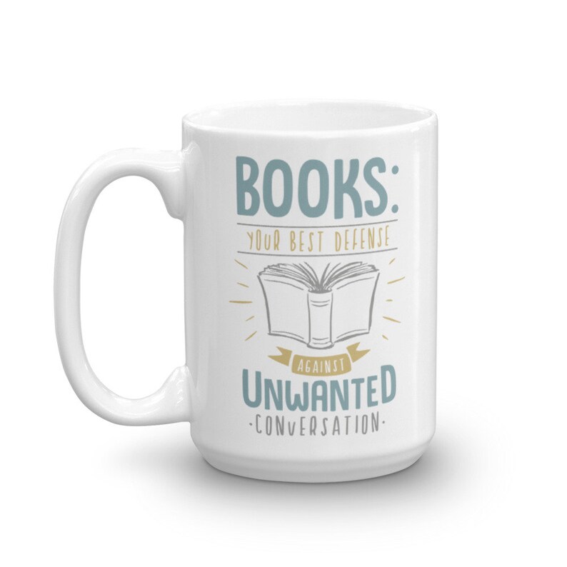 Puede incluir: Taza de cer&aacute;mica blanca con un asa grande. La taza presenta el texto "BOOKS: YOUR BEST DEFENSE AGAINST UNWANTED CONVERSATION" en letras azules y doradas, con una ilustraci&oacute;n de un libro abierto.