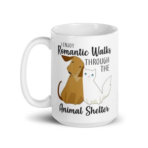 May include: White ceramic coffee mug with a brown dog and white cat illustration. The text reads "I enjoy romantic walks through the animal shelter".