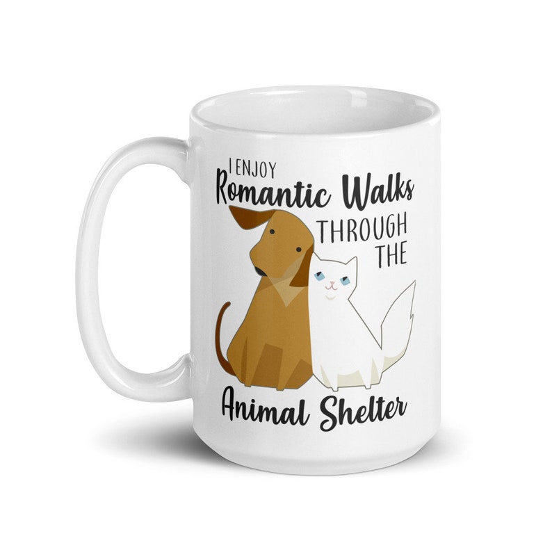 May include: White ceramic coffee mug with a brown dog and white cat illustration. The text reads "I enjoy romantic walks through the animal shelter".