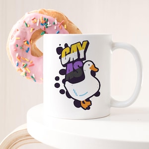 May include: White ceramic mug with a cartoon goose and the text "Gay as" in a colorful font. The text is in a rainbow color scheme with yellow, purple, and black.