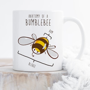 May include: White ceramic mug with a black and yellow cartoon bumblebee illustration. The text "Anatomy of a Bumblebee" is at the top of the mug. The words "Blebbee" and "Bum" are written below the bumblebee.