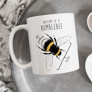 May include: White ceramic mug with a black and white illustration of a bumblebee. The text "Anatomy of a Bumblebee" is printed on the mug. The bumblebee's body parts are labeled "Bum" and "Bleebee".