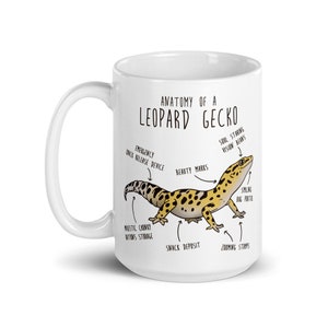 Puede incluir: Una taza de cer&aacute;mica blanca con una ilustraci&oacute;n de dibujos animados de un gecko leopardo y un diagrama anat&oacute;mico humor&iacute;stico. El texto dice "Anatom&iacute;a de un gecko leopardo" y etiqueta las caracter&iacute;sticas del gecko, como "Dispositivo de liberaci&oacute;n r&aacute;pida de emergencia", "Marcas de belleza", "Visi&oacute;n de ojos del alma", "Portal de insectos sonriente", "Almacenamiento de raciones regordetas majestuosas", "Dep&oacute;sito de refrigerios" y "Troncos de zoom".