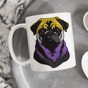 Peut inclure: Mug en céramique blanche avec une illustration de carlin stylisé. Le carlin a un visage noir, des oreilles jaunes et un col violet. La tasse a une grande anse incurvée et est posée sur une surface grise.