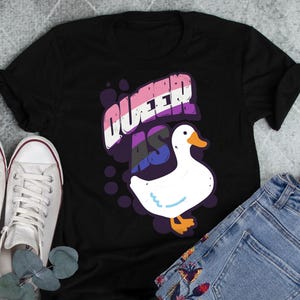May include: Black t-shirt with the text "Queer as" in rainbow colors and a white goose graphic.