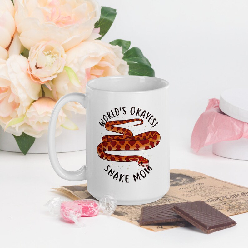May include: White ceramic mug with a brown snake illustration and the text "World's Okayest Snake Mom".