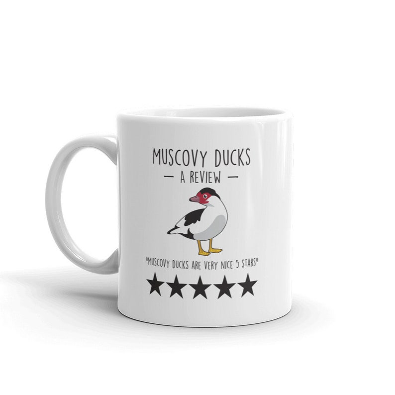 May include: White ceramic mug with a black and white illustration of a Muscovy duck. The text "Muscovy Ducks - A Review -" is printed on the mug. Below the duck is the text "Muscovy Ducks are very nice 5 stars" and five black stars.