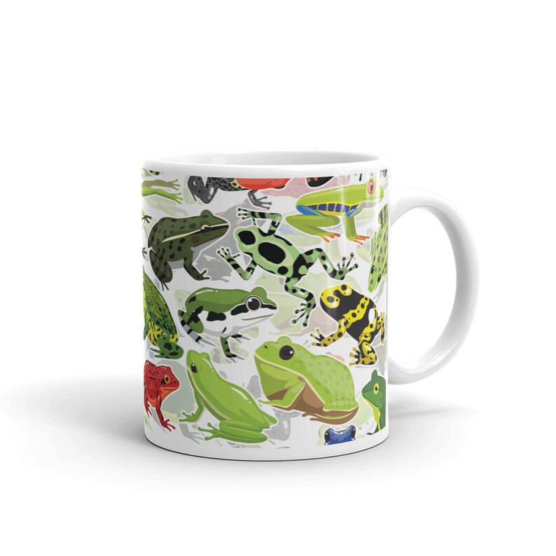 May include: White ceramic mug with a colorful pattern of frogs. The frogs are green, blue, yellow, red, and black. The mug has a white handle.