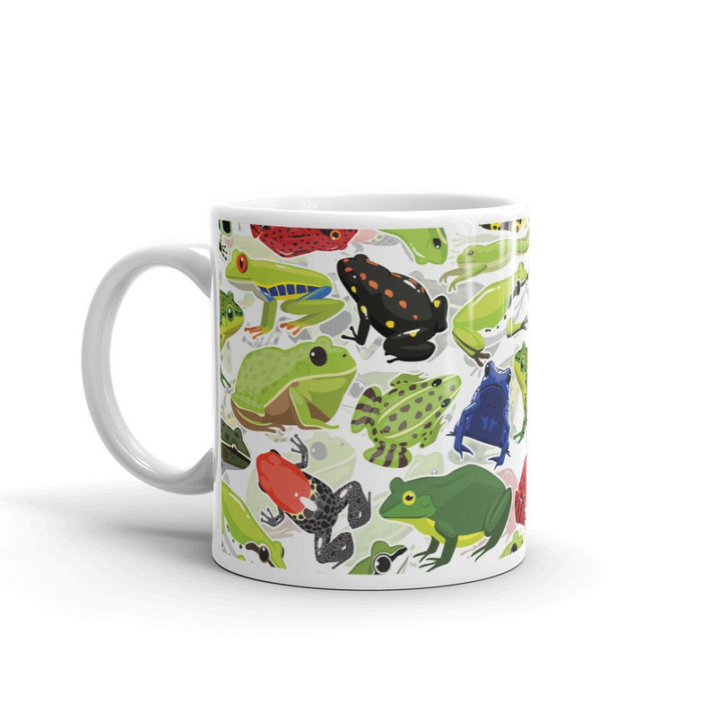 May include: White ceramic mug with a colorful pattern of frogs. The frogs are green, red, blue, black, and yellow. The mug has a white handle.