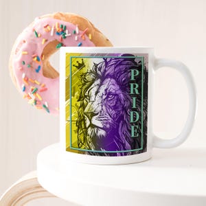 Puede incluir: Taza de cerámica blanca con un gráfico de león morado, amarillo y verde y la palabra "PRIDE" en texto verde.