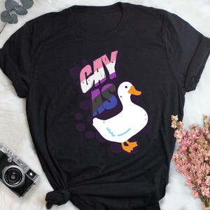 May include: Black t-shirt with a white goose and the text "gay as" in rainbow colors.