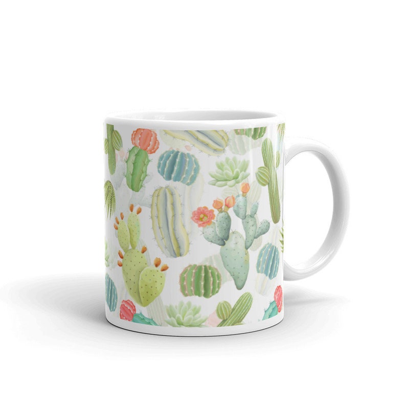 May include: White ceramic mug with a pattern of green, pink, and yellow cacti and succulents. The mug has a white handle.