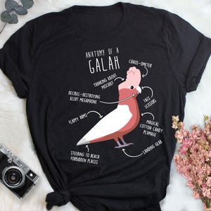 May include: Black t-shirt featuring a diagram of a Galah, a type of cockatoo, with labeled parts like "Flappy Arms" and "Magical Cotton Candy Plumage." The text "Anatomy of a Galah" is at the top. A fun, whimsical design.
