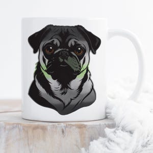 Puede incluir: Taza de cerámica blanca con una ilustración detallada de un perro pug. El pug tiene un pelaje negro, ojos marrones y un acento verde alrededor del cuello. La taza tiene un asa blanca y está sobre una superficie de madera.