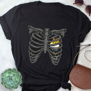 May include: Black t-shirt featuring a graphic of a ribcage with a rainbow heart inside. The heart is dripping with paint.