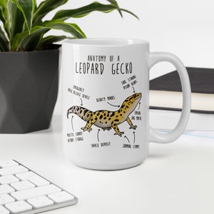 Puede incluir: Taza de cer&aacute;mica blanca con una ilustraci&oacute;n de dibujos animados de un gecko leopardo y el texto "Anatom&iacute;a de un gecko leopardo". La ilustraci&oacute;n muestra las partes del cuerpo del gecko etiquetadas con nombres humor&iacute;sticos como "Dispositivo de liberaci&oacute;n r&aacute;pida de emergencia", "Marcas de belleza", "Dep&oacute;sito de refrigerios" y "Sellos de zoom".