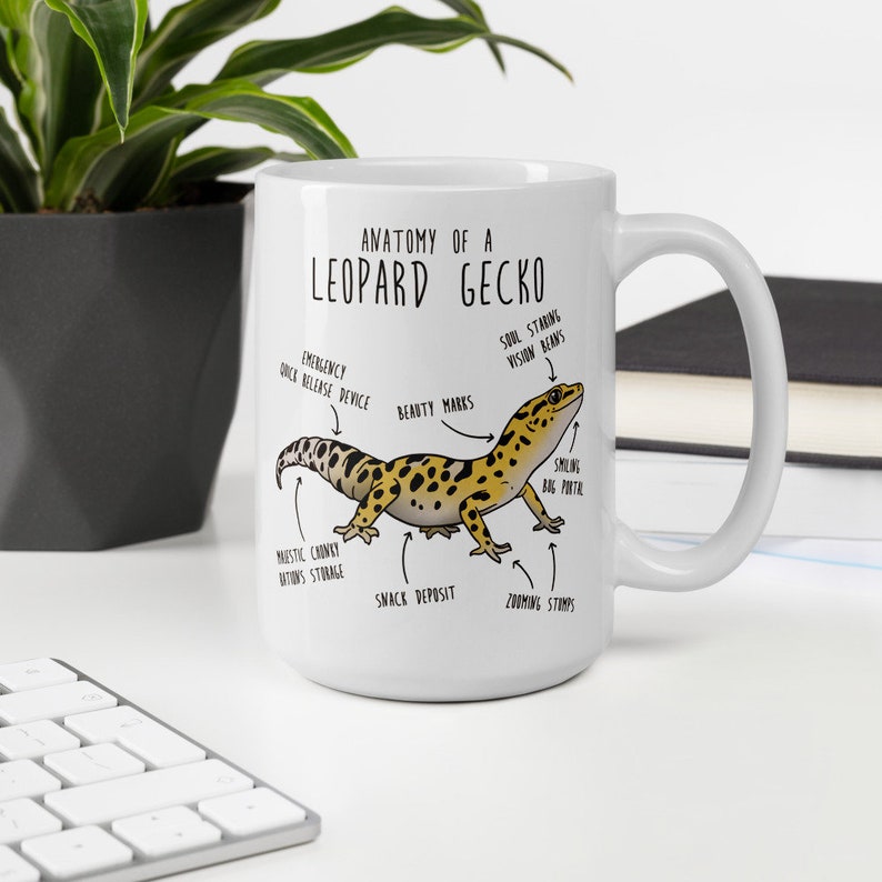 Puede incluir: Taza de cer&aacute;mica blanca con una ilustraci&oacute;n de dibujos animados de un gecko leopardo y el texto "Anatom&iacute;a de un gecko leopardo". La ilustraci&oacute;n muestra las partes del cuerpo del gecko etiquetadas con nombres humor&iacute;sticos como "Dispositivo de liberaci&oacute;n r&aacute;pida de emergencia", "Marcas de belleza", "Dep&oacute;sito de refrigerios" y "Sellos de zoom".