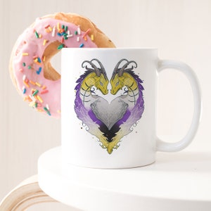 May include: White ceramic mug featuring a design of two yellow and gold dragons forming a heart shape with purple and black accents. The dragons are facing each other and their tails are intertwined.