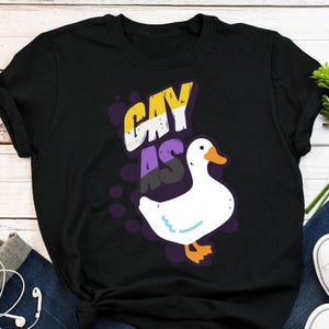 May include: Black t-shirt with a white goose and the text "Gay as" in purple, yellow, and black lettering.