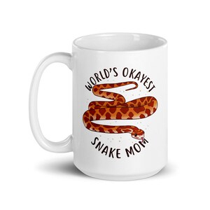 May include: White ceramic mug with a brown and orange snake illustration and the text "World's Okayest Snake Mom".