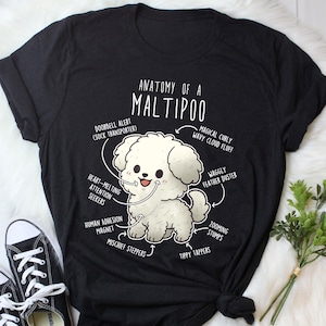 Könnte beinhalten: Schwarzes T-Shirt mit einer Cartoon-Illustration eines Maltipoo-Hundes und anatomischen Beschriftungen. Der Text lautet "Anatomie eines Maltipoo" mit Beschriftungen wie "Magical Curly Wavy Cloud Fluff" und "Heart-Melting Attention Seekers".