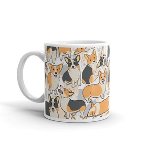 May include: White ceramic mug with a pattern of cartoon corgis in black, orange, and white. The corgis are in various poses, including sitting, standing, and running.