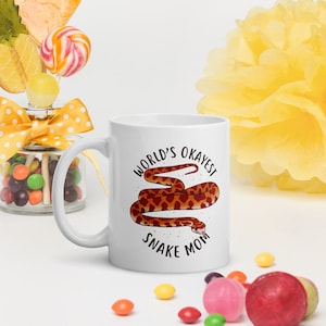 May include: White ceramic mug with a brown snake illustration and the text "World's Okayest Snake Mom".