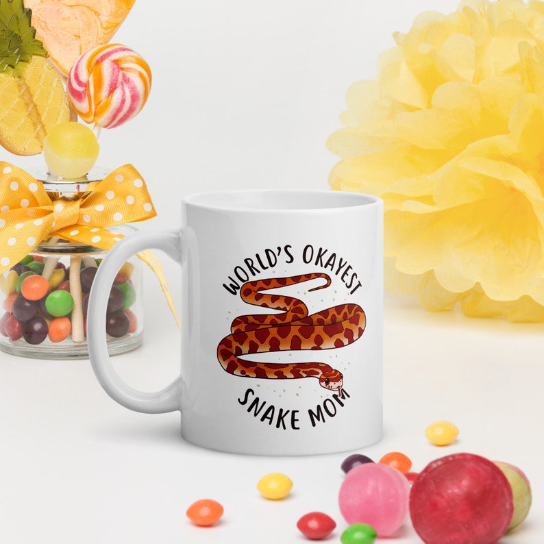 May include: White ceramic mug with a brown snake illustration and the text "World's Okayest Snake Mom".