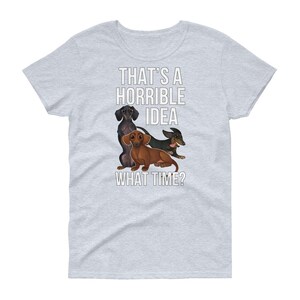 May include: A light gray t-shirt with a white graphic of three dachshund dogs. The text "That's a horrible idea. What time?" is printed on the shirt.