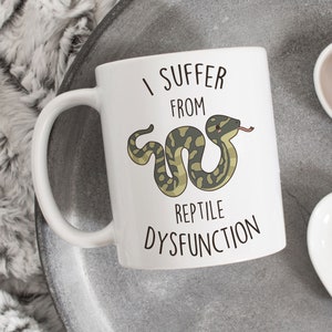 May include: White ceramic mug with a black handle. The mug features the text "I Suffer From Reptile Dysfunction" and a cartoon snake illustration in green, brown, and red.