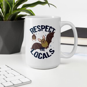 May include: White ceramic coffee mug with a blue and brown graphic of bats and the text "Respect the Locals".