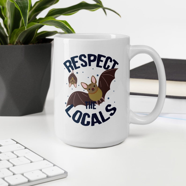 May include: White ceramic coffee mug with a blue and brown graphic of bats and the text "Respect the Locals".