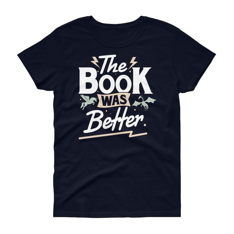 Pode incluir: Uma camiseta azul marinho com texto branco que diz "The Book Was Better" com um raio estilizado antes e depois de "The" e um raio estilizado abaixo de "Better". H&aacute; um unic&oacute;rnio branco e um drag&atilde;o verde de cada lado do texto.