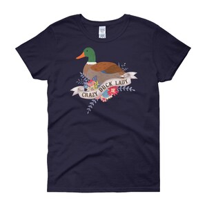 Puede incluir: Una camiseta azul marino con un gr&aacute;fico de un pato verde y marr&oacute;n con flores y el texto "Crazy Duck Lady".