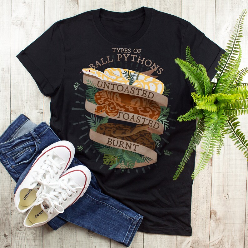 Może przedstawiać: Czarny T-shirt z grafiką przedstawiającą trzy pytony kr&oacute;lewskie z tekstem "Types of Ball Pythons" i słowami "Untoasted", "Toasted" i "Burnt" na grafice.